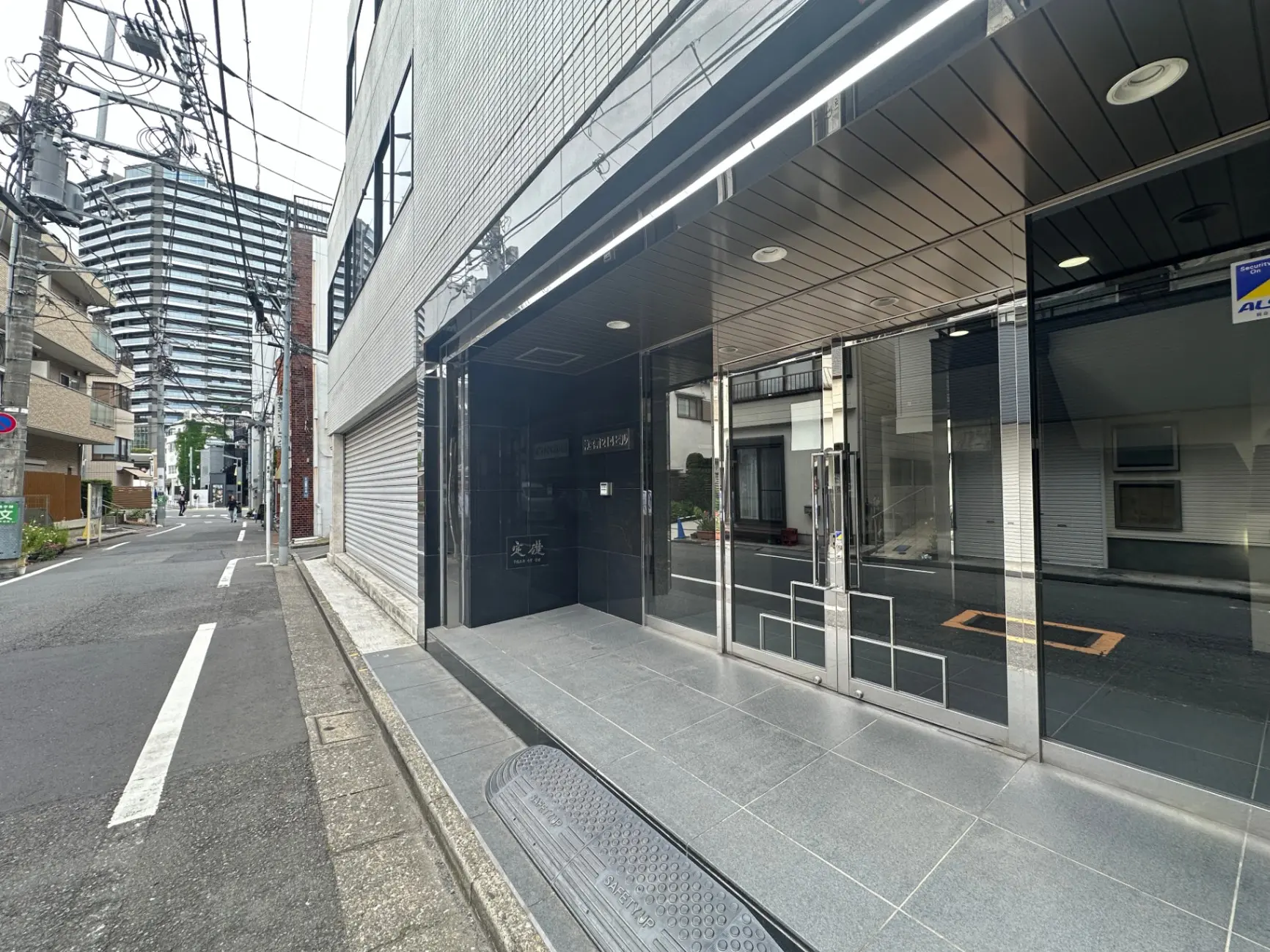 日本の都市部の通りに面したモダンな建物の外観、ガラス張りのエントリーウェイと歩道