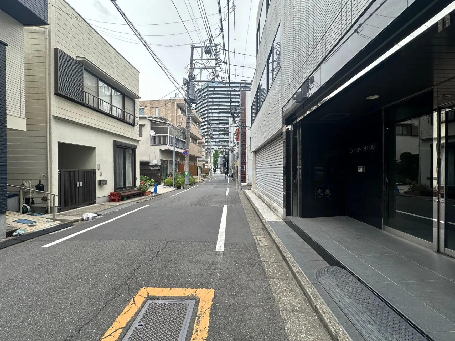 日本の都市風景、狭いアスファルト道路、周囲に建つ住宅と店舗、空に向かって伸びる電線