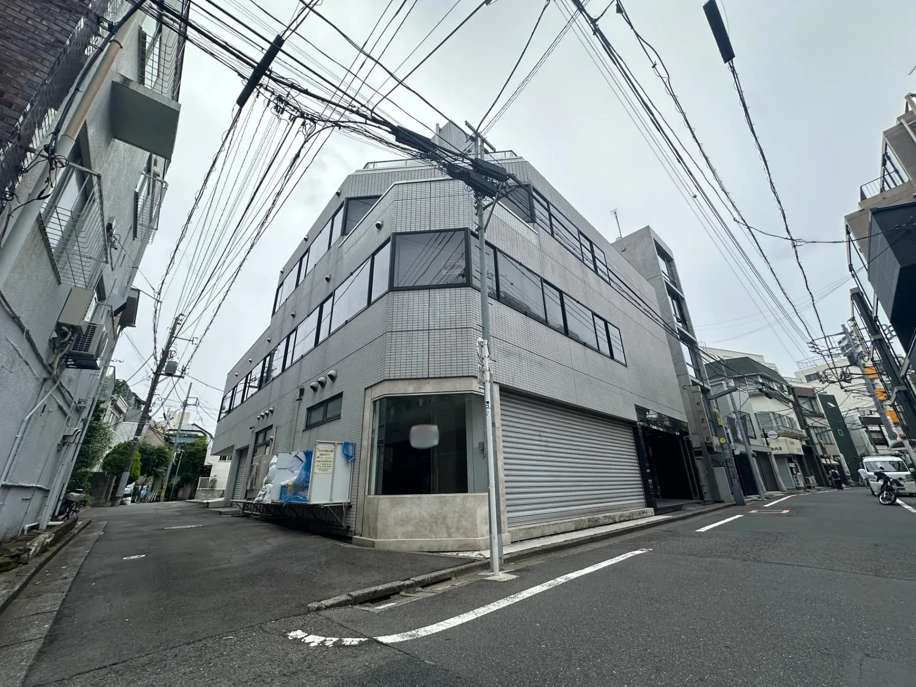 都市のコーナーに位置する現代的な建物、シャッター付きのガレージと複数の電線が交差する街角