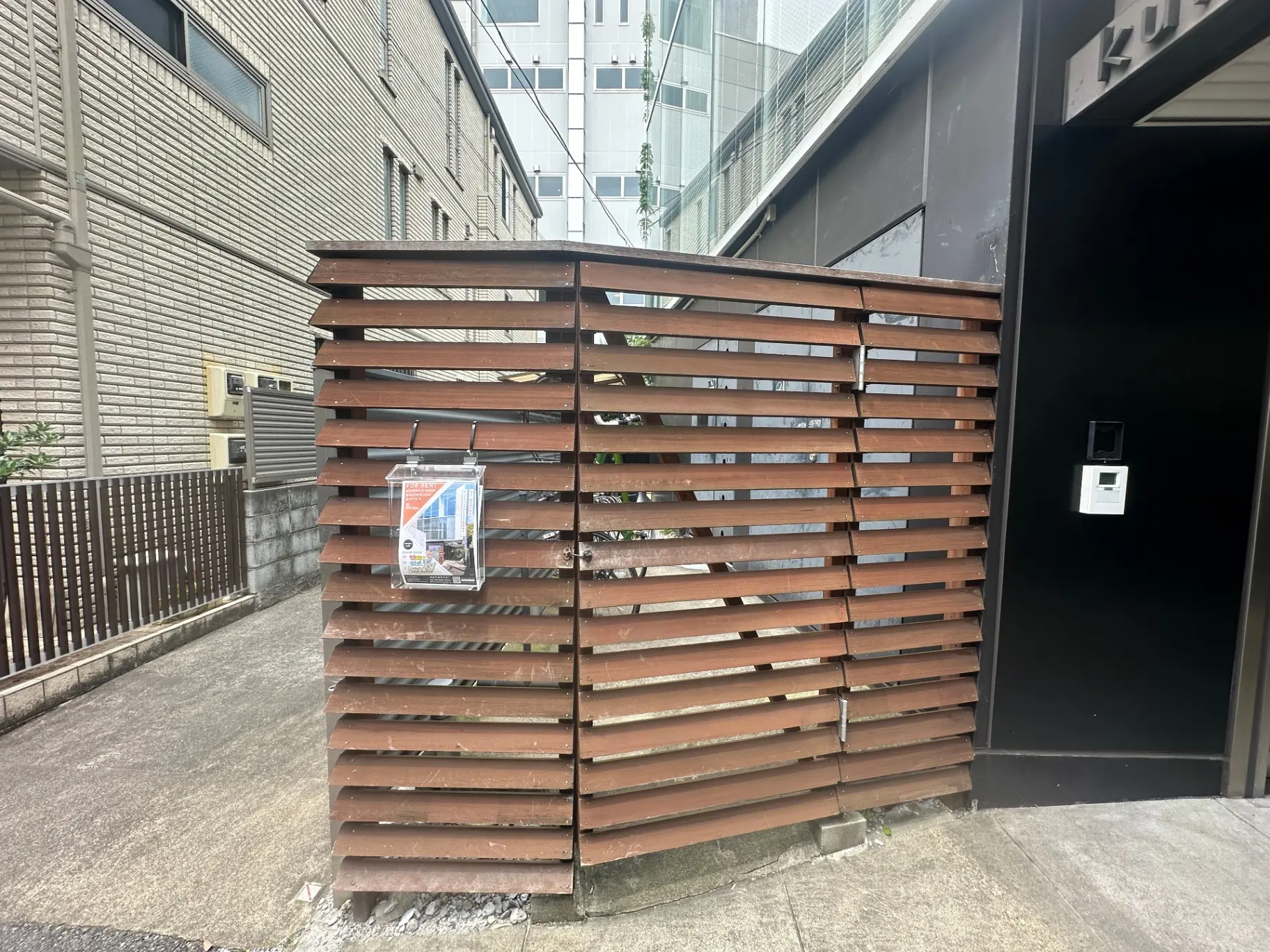 建物の外観に隣接する木製の格子デザインのごみ集積所、都市景観に溶け込むクリーンなデザイン