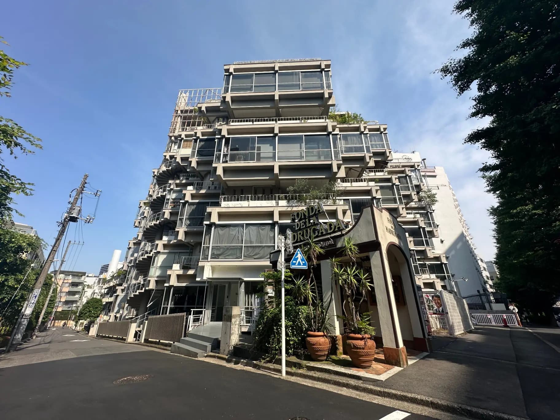 現代的な外観のマンションと青空、植物が飾られたエントランス、都市の住宅街