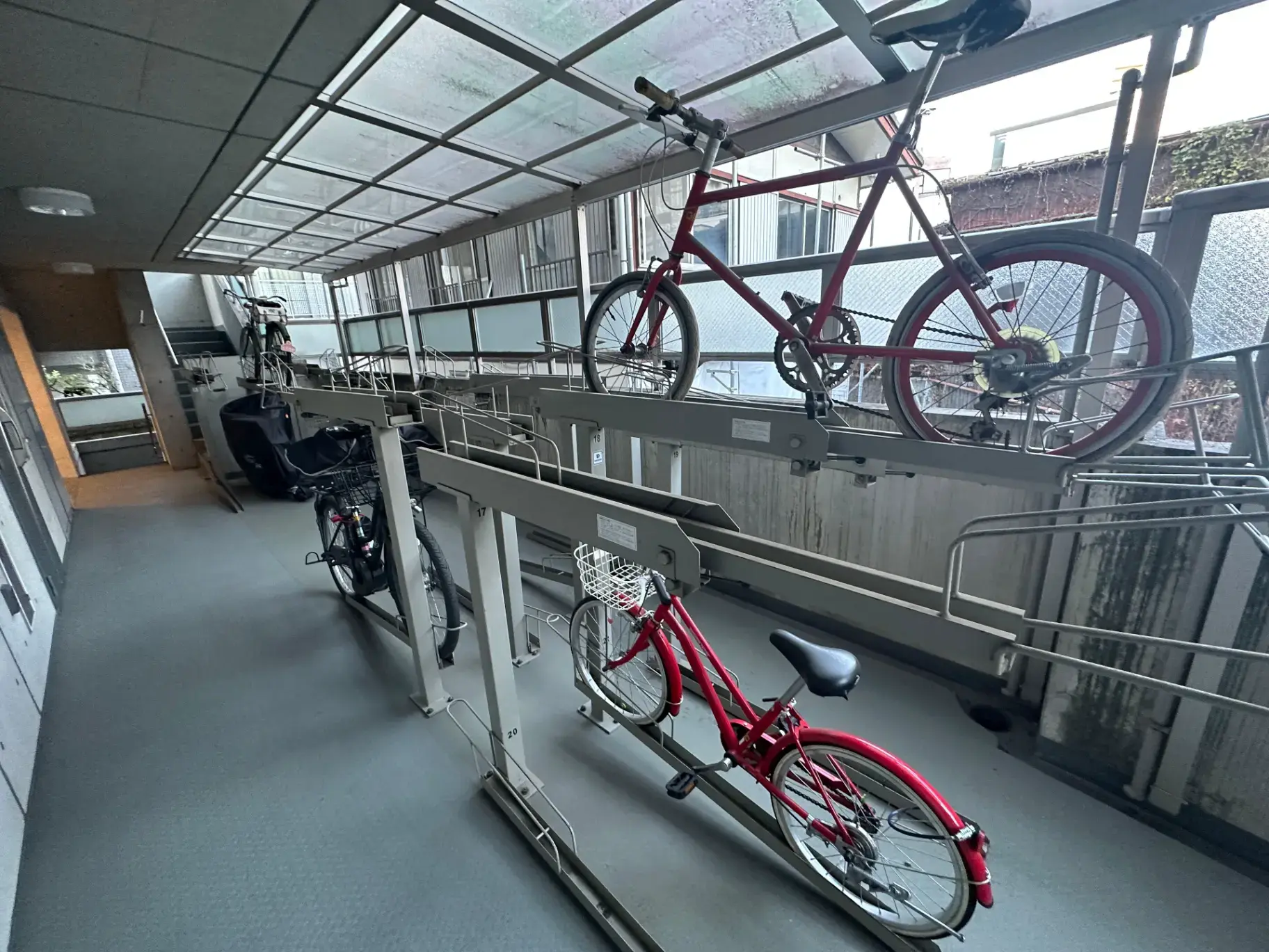 屋内自転車駐輪場の風景、壁掛け式駐輪ラックに収納された赤い自転車が見える