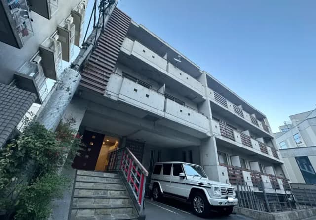 都市部に位置するコンクリート造りのマンションと階段、駐車された白のSUV車