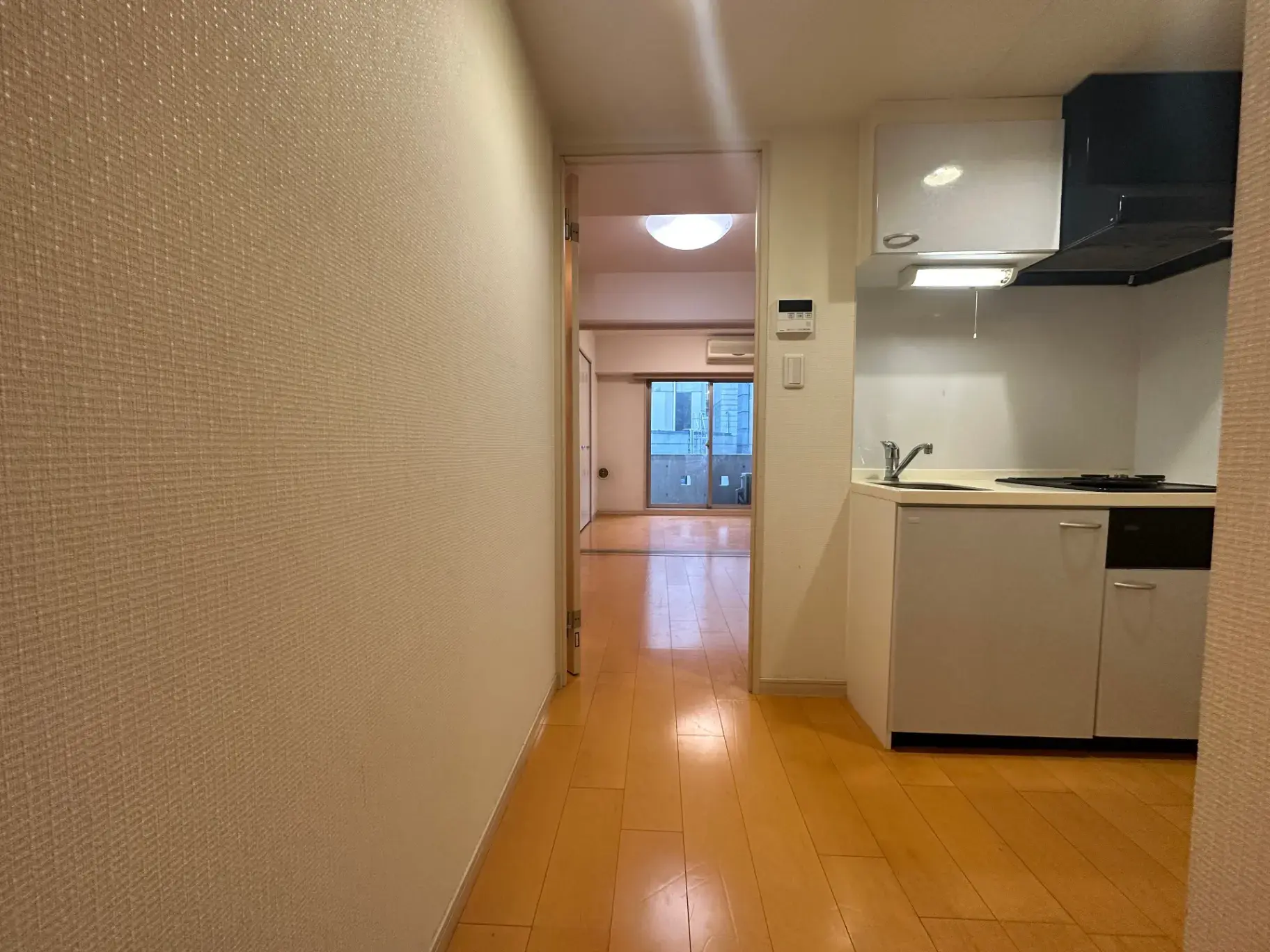 シンプルなデザインのキッチンと続く広々したリビングルーム、タイルフローリング、明るい照明のあるマンションインテリア