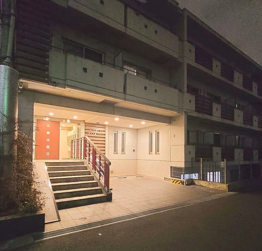 夜景の中のマンションの入り口、階段とオレンジ色のドアが特徴的な外観デザイン