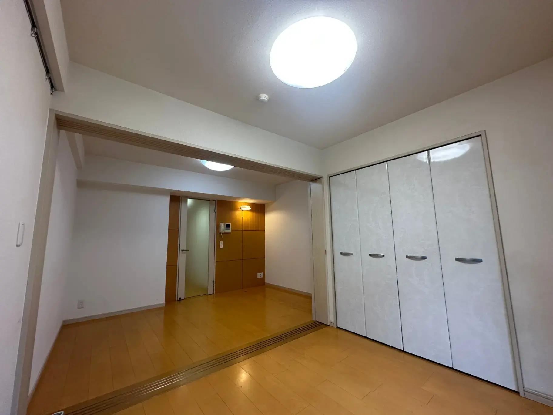シンプルなデザインの空の部屋、木製フロアと白い壁面クローゼット、天井のライトが明るさを提供