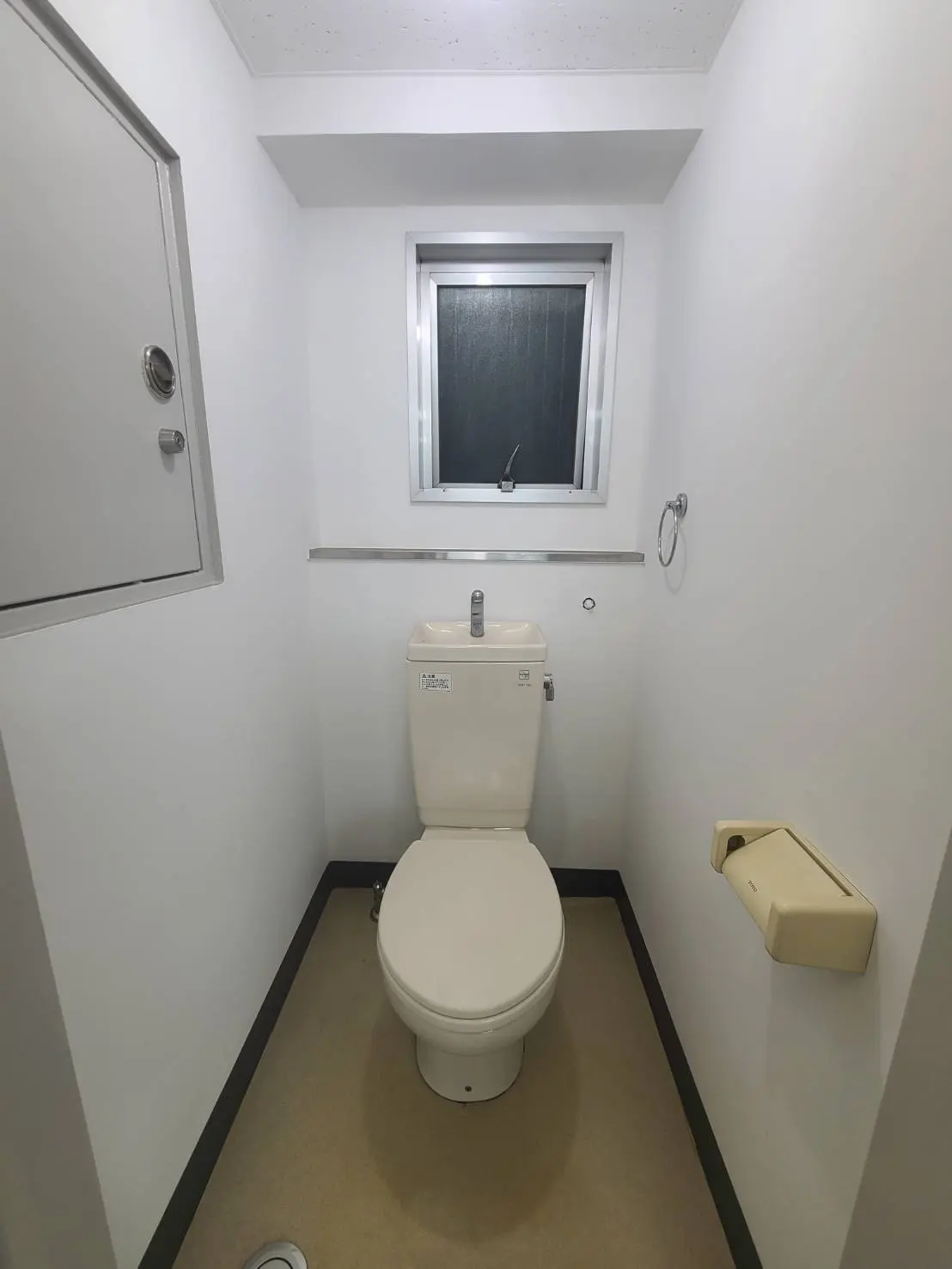 シンプルなデザインのトイレルーム、白い壁と便器、小窓と照明のある清潔感のある空間