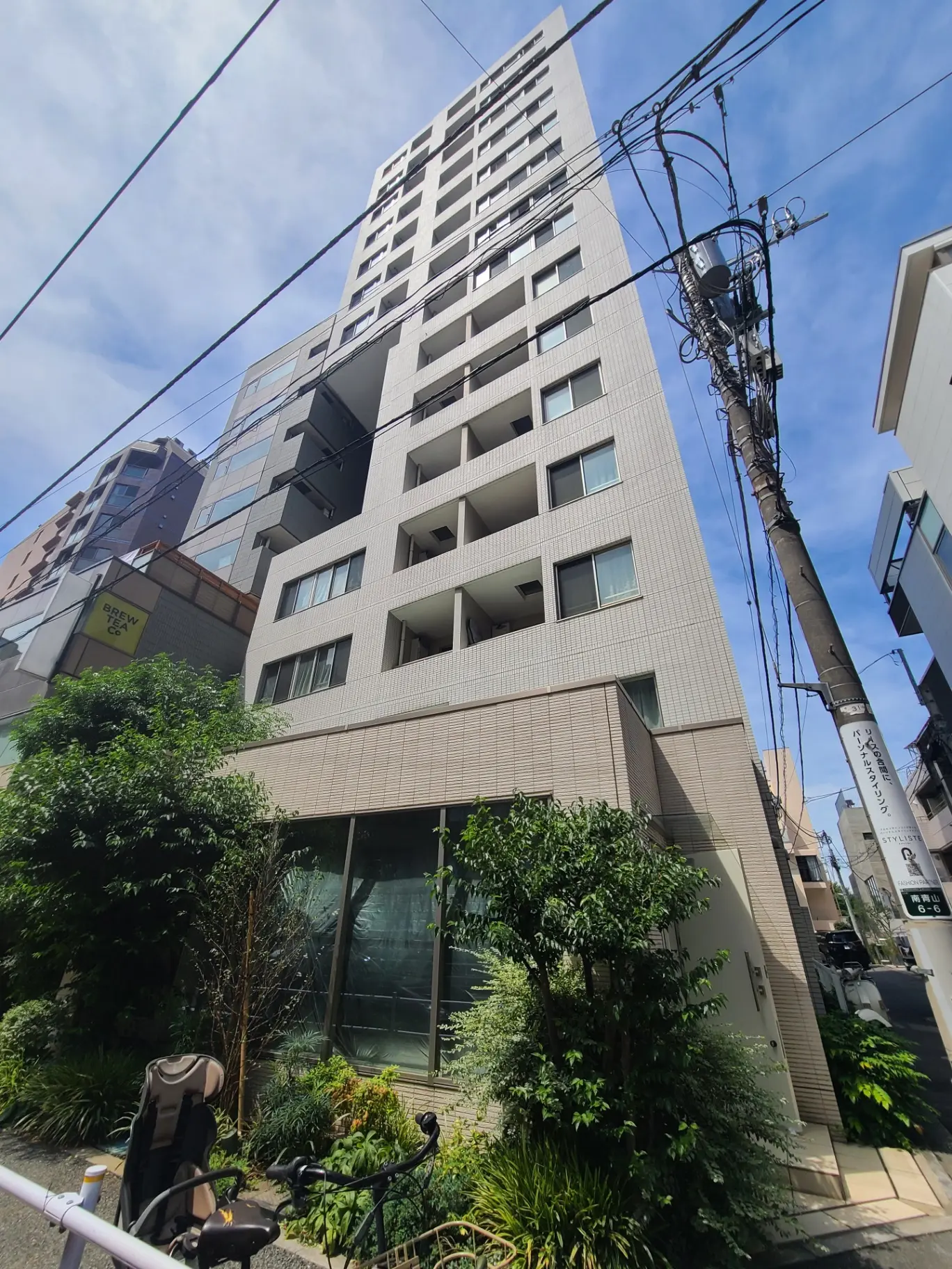 現代的なマンションの外観、青空に映える高層ビルディング、都市の植栽と自転車が見える街並み