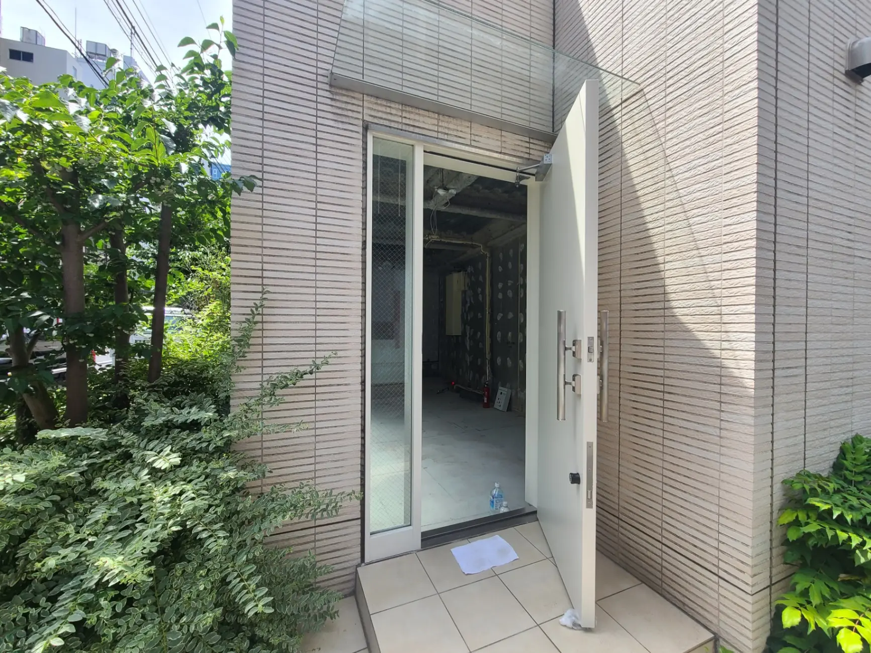 現代的な建物の玄関、開いたガラス扉、緑豊かな外植えの植物
