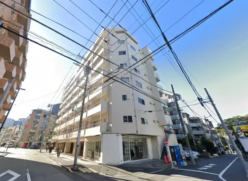 日本の都市部に位置するモダンなマンションの外観、歩行者と交通標識が見える晴れた日の街角