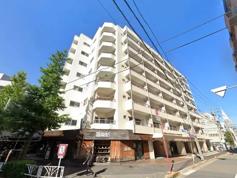 都市の日当たりの良い一角に位置する白い外壁のマンション、１階のカフェ店舗付き、歩行者が通る歩道