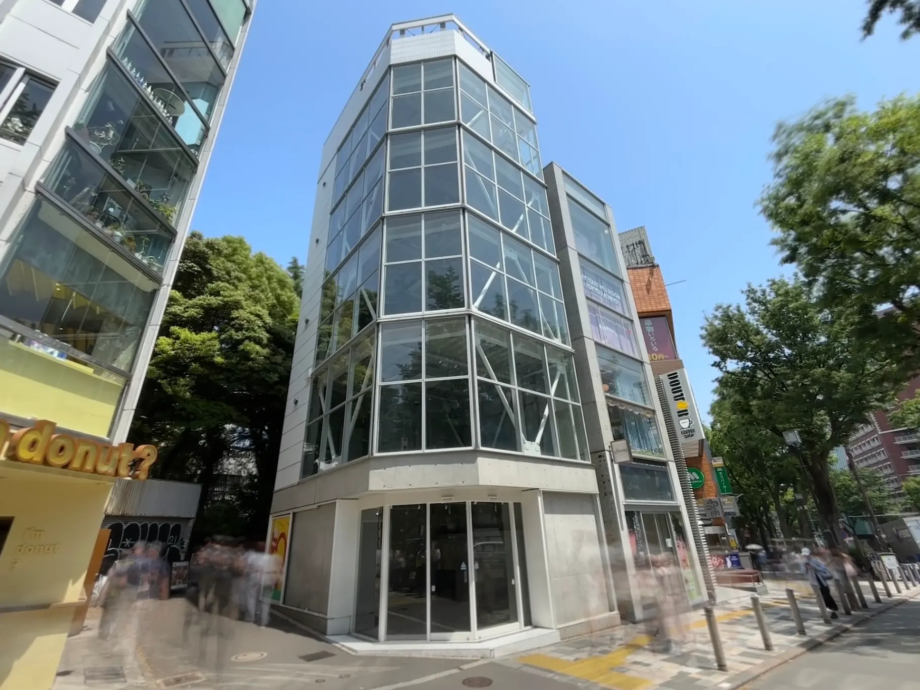- 近代的なガラス張りのビルとその周囲の街並み、青空と樹木を背景にした都市の風景