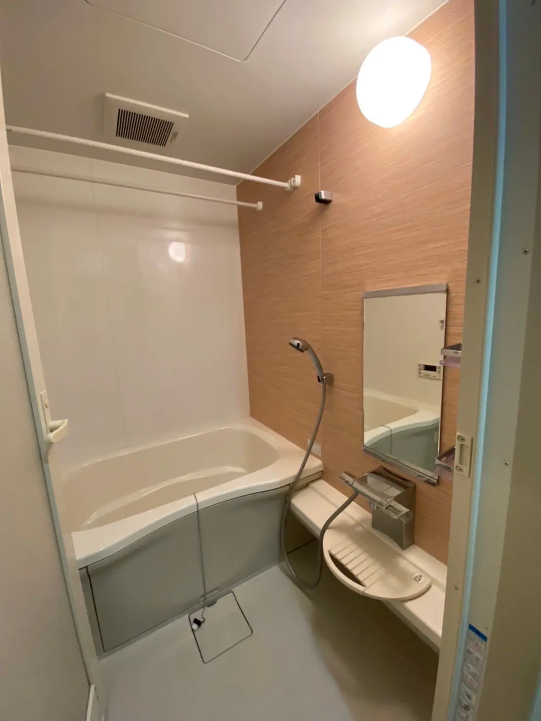 コンパクトなモダン風呂・トイレ一体型、浴槽とシャワー、木目調タイル、照明が明るいバスルーム