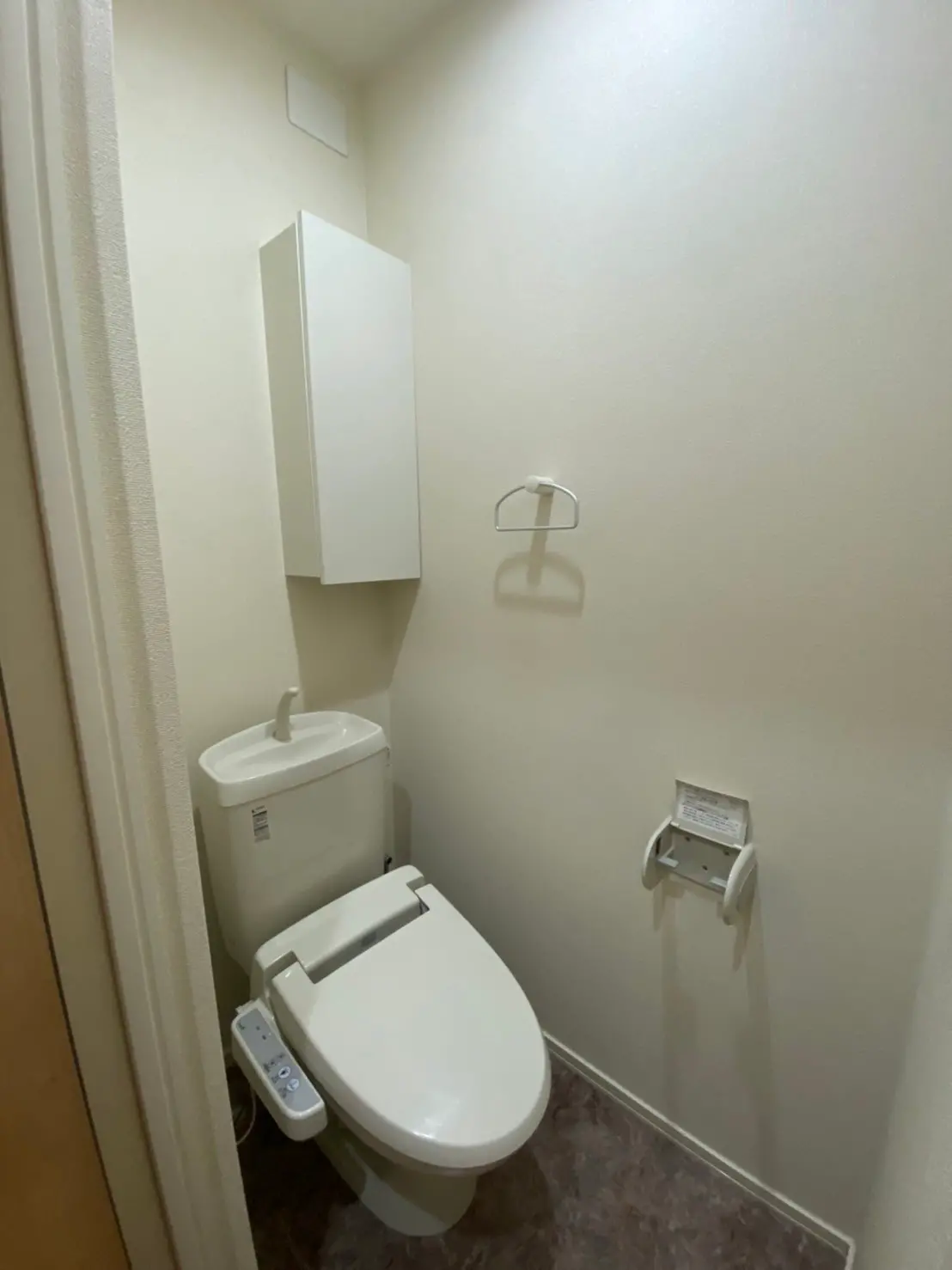 シンプルなデザインのトイレ、ウォシュレット付き便座とトイレットペーパーホルダー、白い壁とマーブル調の床