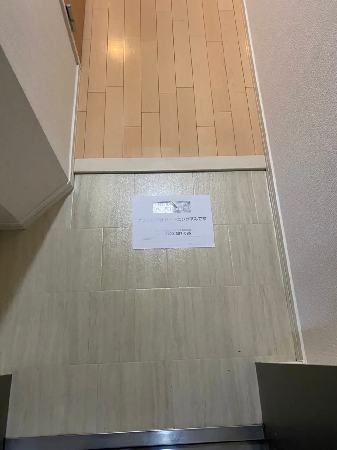 玄関の壁に掲示された不動産連絡先情報、木目調タイルの床