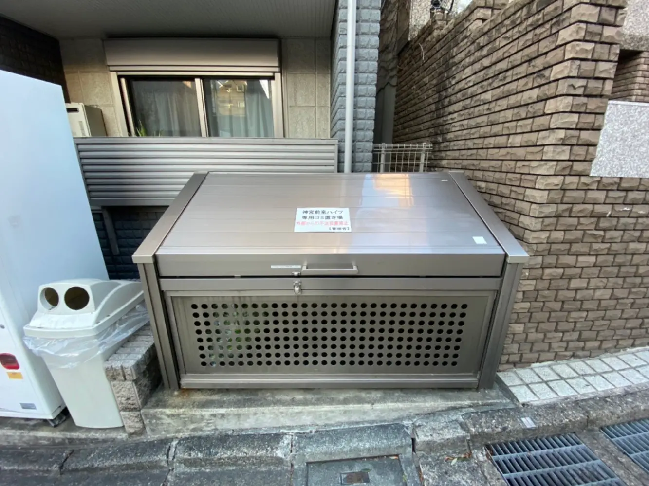 都市環境に設置されたステンレス製のゴミ箱とリサイクルステーション、ブロック塀と舗装された歩道