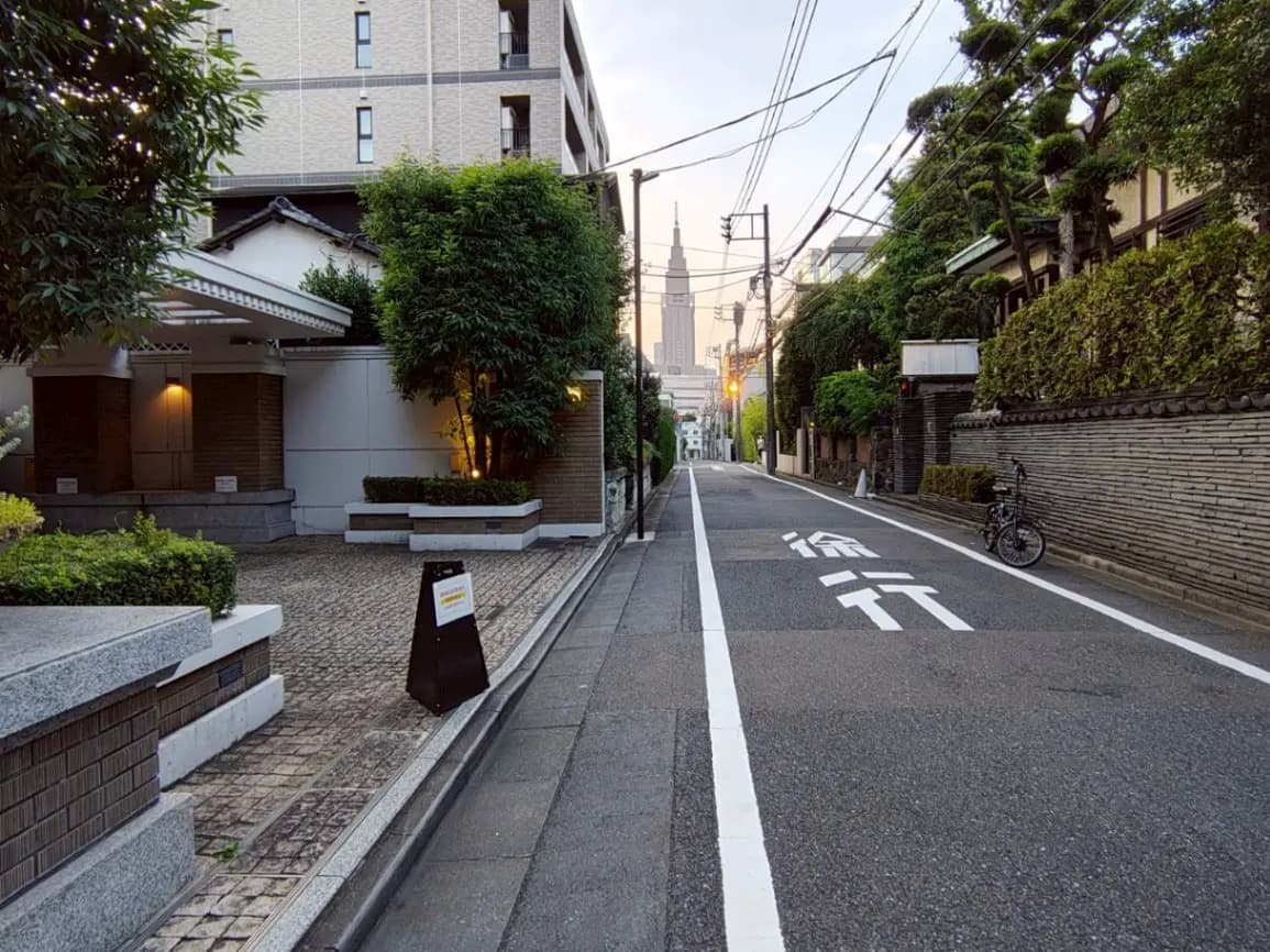 - 東京の静かな街並み、石畳のある道と緑の木々、遠くに見える東京スカイツリーのシルエット