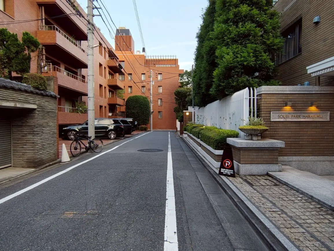 - ハリウッドスタイルのアパートメントが並ぶ静かな通り、舗装された道路と整備された植栽、目立つ駐車場の標識がある風景