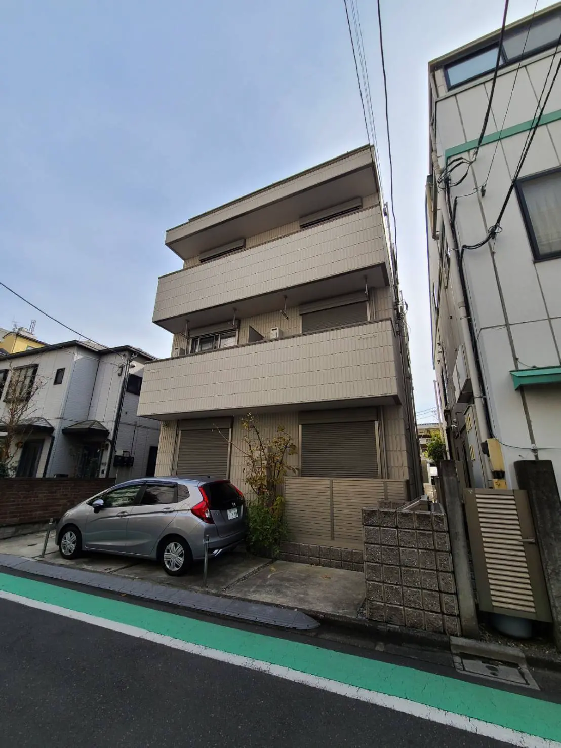現代的な外観の都市型アパートメントビルと駐車スペースに停車しているグレーのコンパクトカー