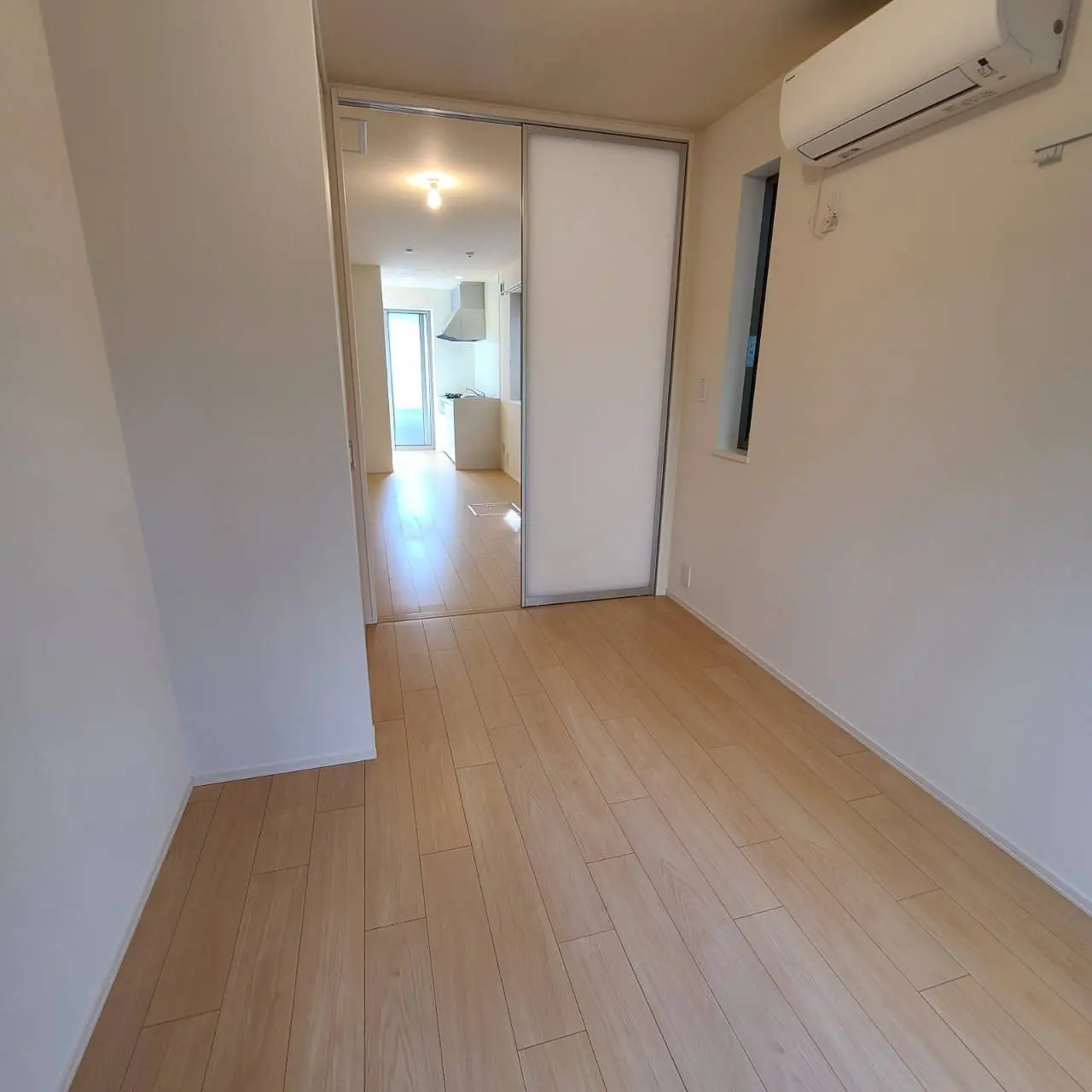 明るい照明と木製フローリングのあるシンプルでモダンな部屋、右側にエアコンと小窓が見えるインテリア