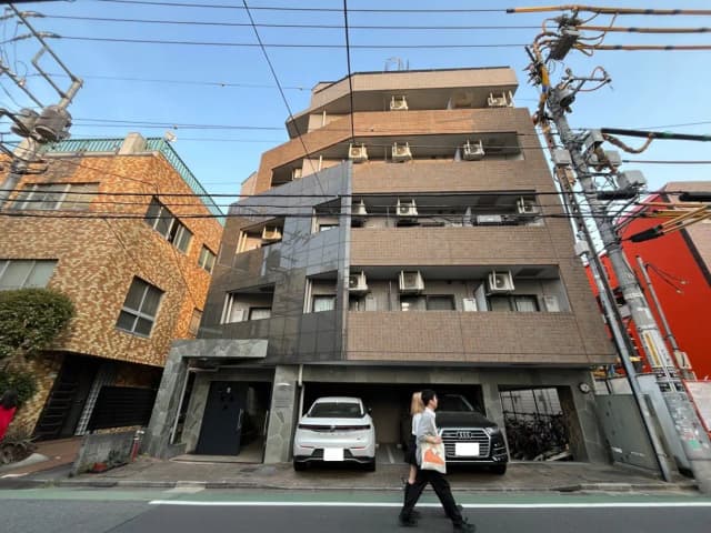 日本の都市風景、歩道を歩く人、背景に複数のアパート建物と車、電線と青空