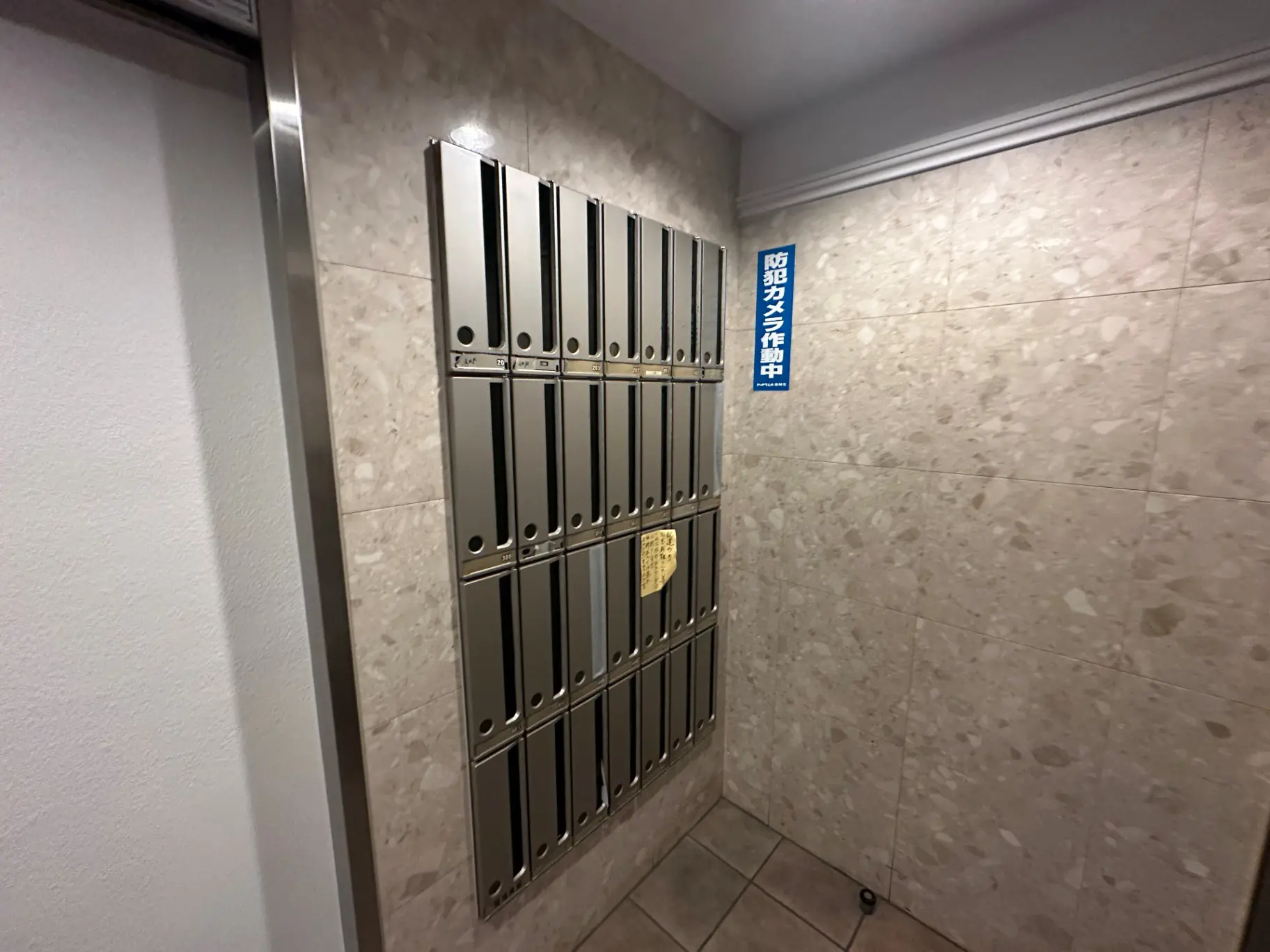 室内の郵便受けボックスと宅配ボックスが並んで設置されている廊下、配達物受取案内のサインが壁に掲示