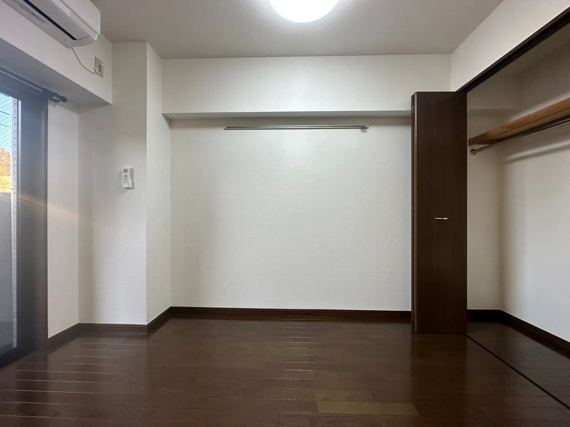 空の洋服ダンスが設置されたシンプルな和室、茶色いフローリングと白い壁、自然光が差し込む窓