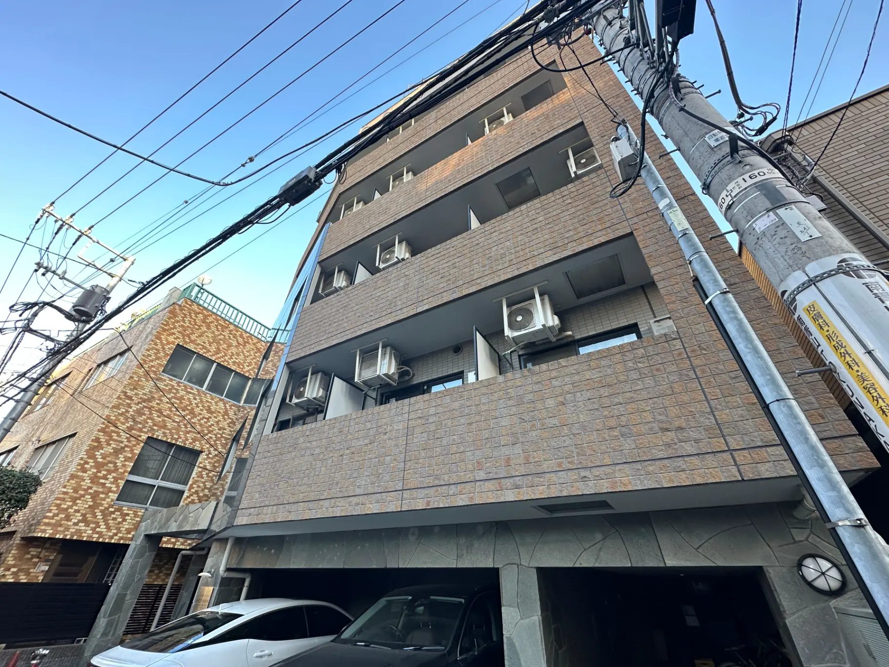 都市の電線が集まる角度から見た現代的なマンション、駐車スペースあり、エアコン室外機が取り付けられたバルコニー