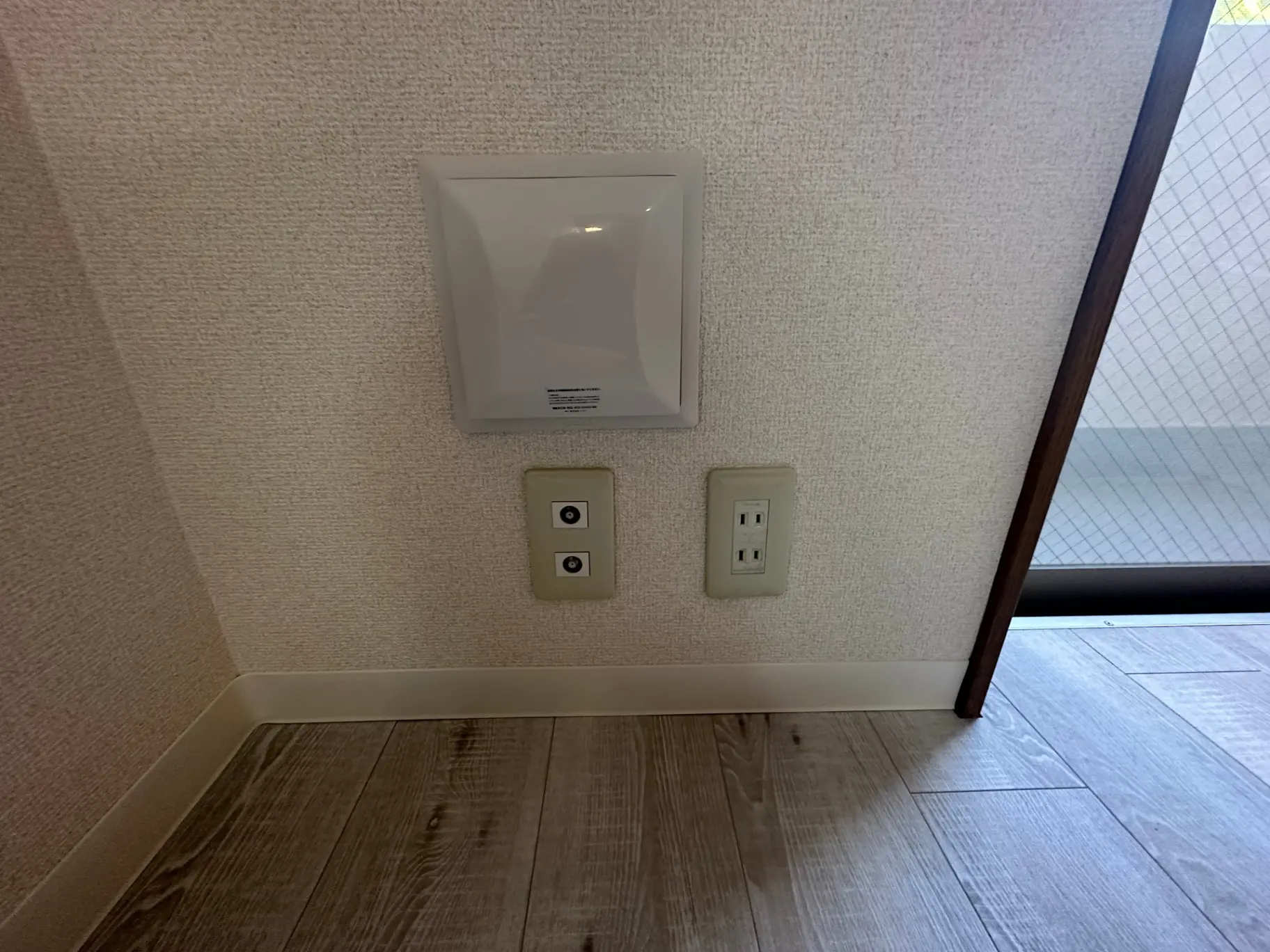 室内の壁に取り付けられたエアコンの温度調整パネルと電源コンセント、木目調のフローリング
