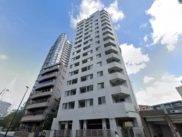 都市部に位置するモダンな高層マンションと周辺街並み、青空と雲が映る窓ガラス