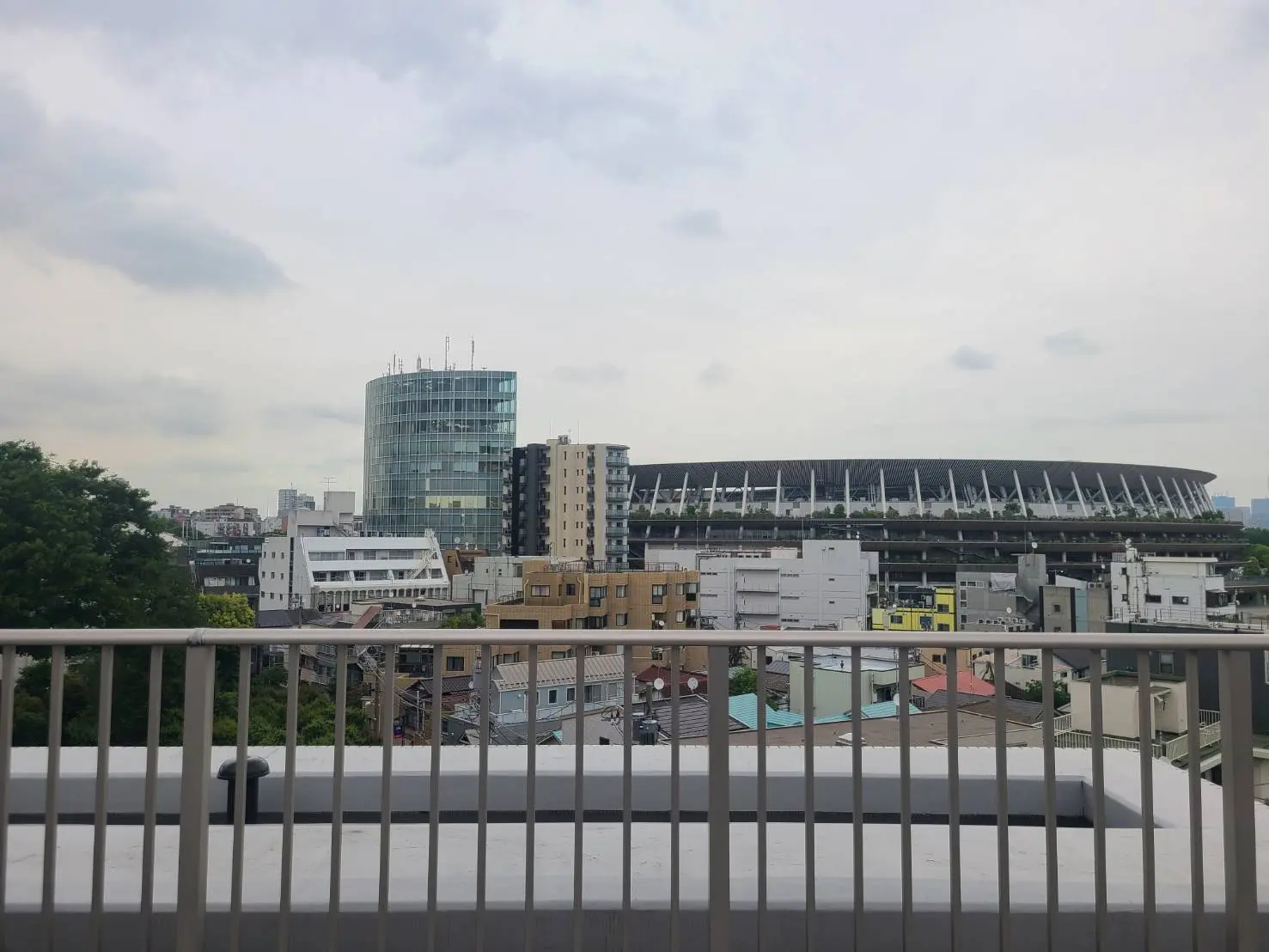 - 都市の風景、現代的なビルとサッカースタジアムが見える屋上からの眺め、緑豊かな木々と多様な建物が並ぶ景観