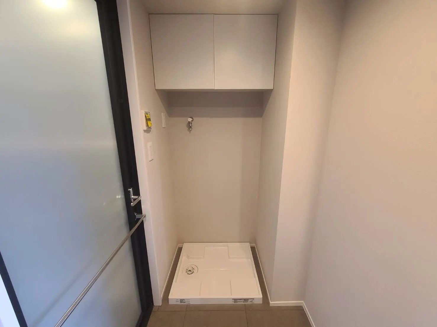 - シンプルなデザインのトイレスペース、上部に収納棚があり、床に排水口付きのトイレ用プレートが設置された明るいインテリア