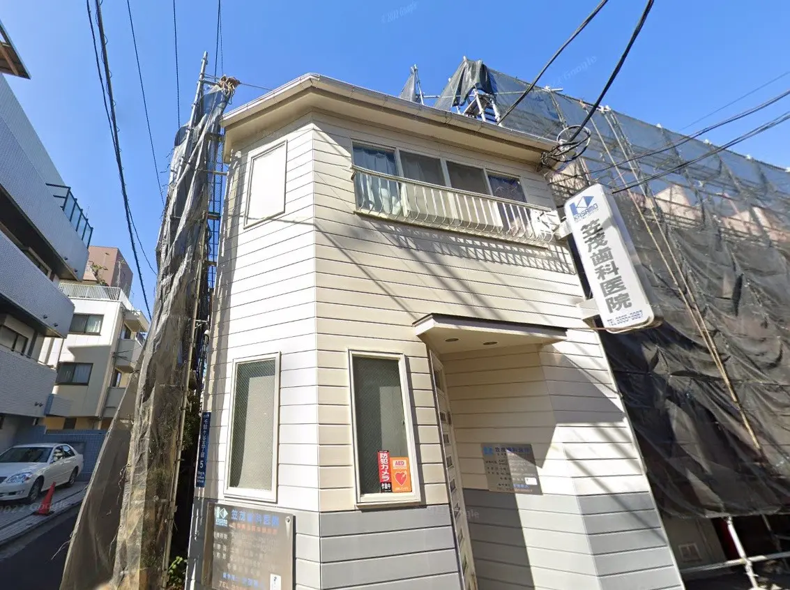 都市の住宅街にある現代的な外観の建物、周囲には電柱と配線が見える、晴れた日の外観