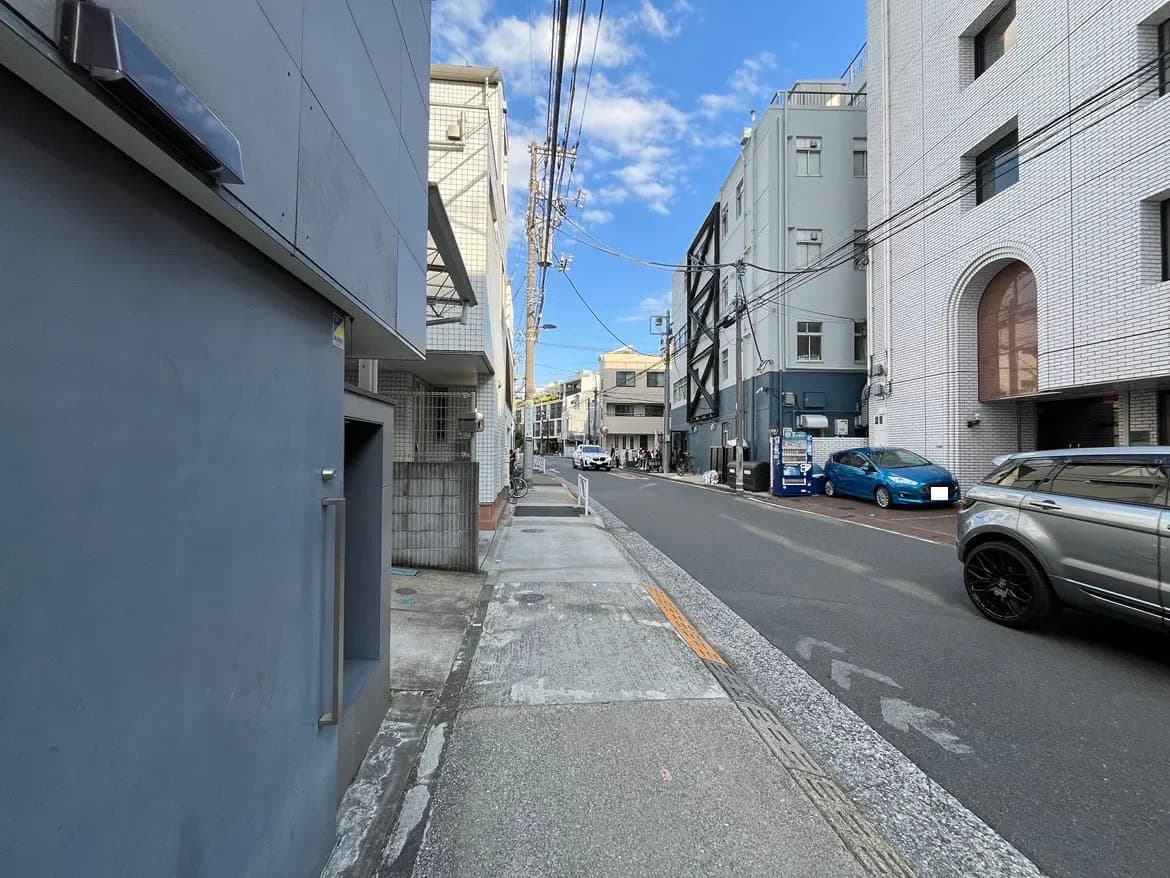 - 都市の静かな通りの風景、両側に建物が並び、晴れた青空の下を自転車と車が通行している様子