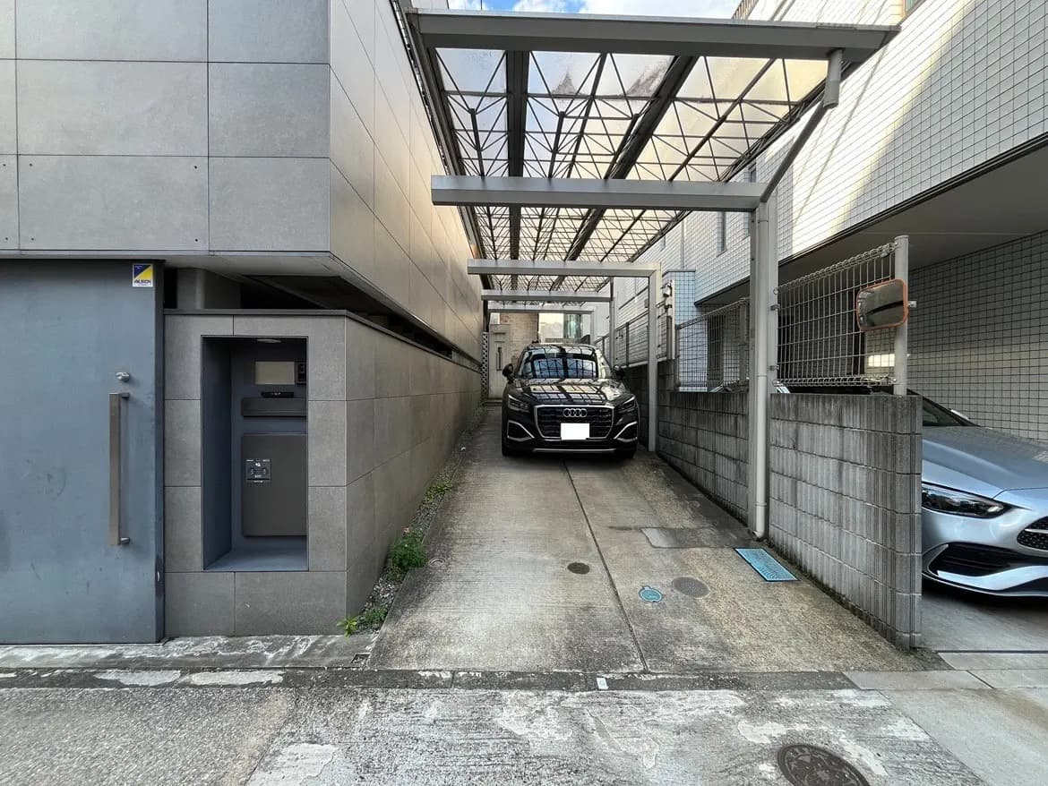 - モダンな住宅の車道、カーポートに停車した黒いアウディのSUVと隣にある銀色の車、整然としたコンクリートの壁と窓のある外観