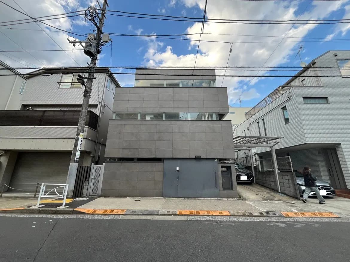 - 現代的な外観の住宅、グレーのタイル装飾、隣接する建物と道路が写った都市の風景