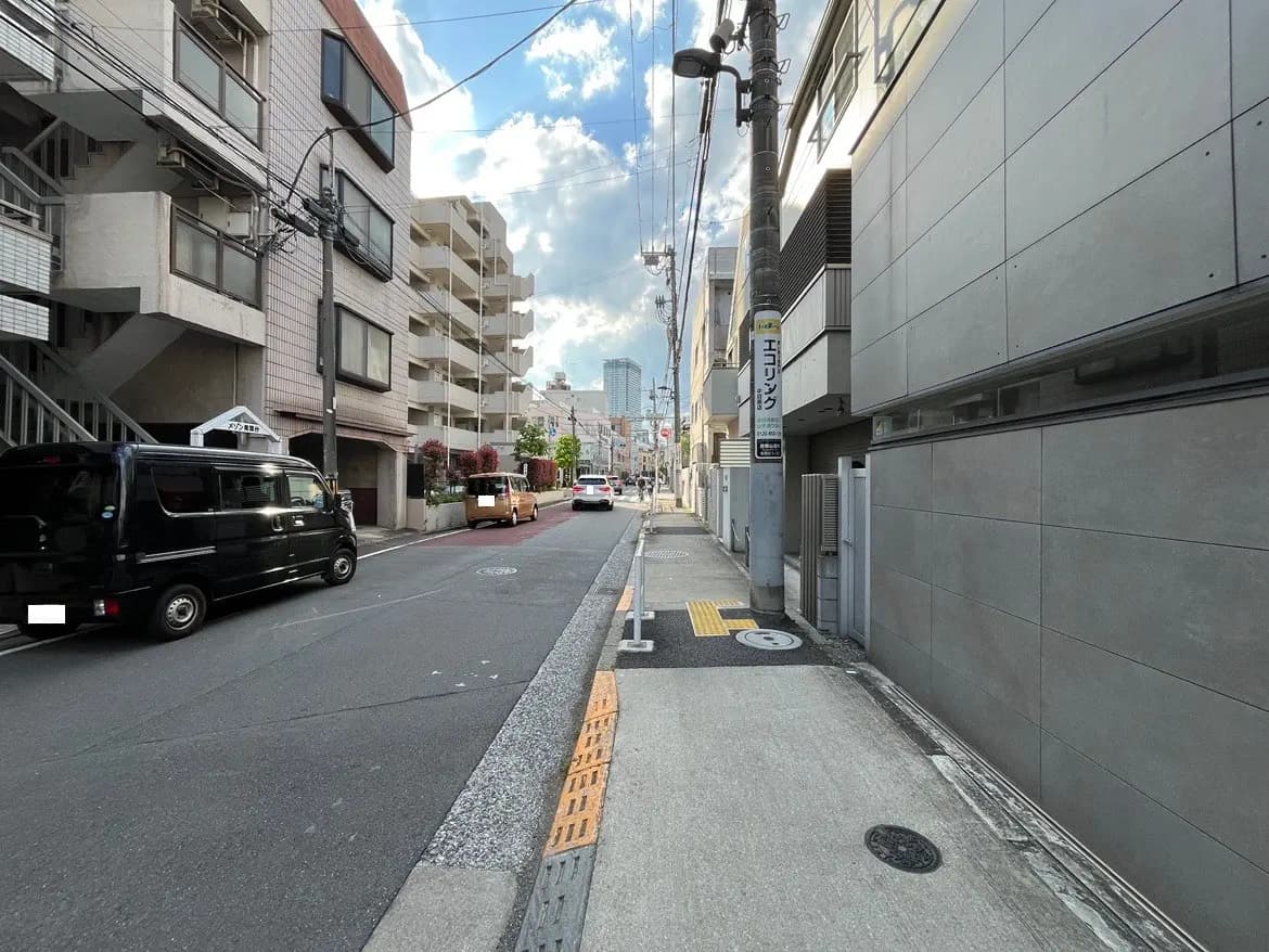 - 都市部の道路沿いにあるアパートメントビル、街灯や車が行き交う風景、青空に浮かぶ雲が広がる登録された場所の眺め