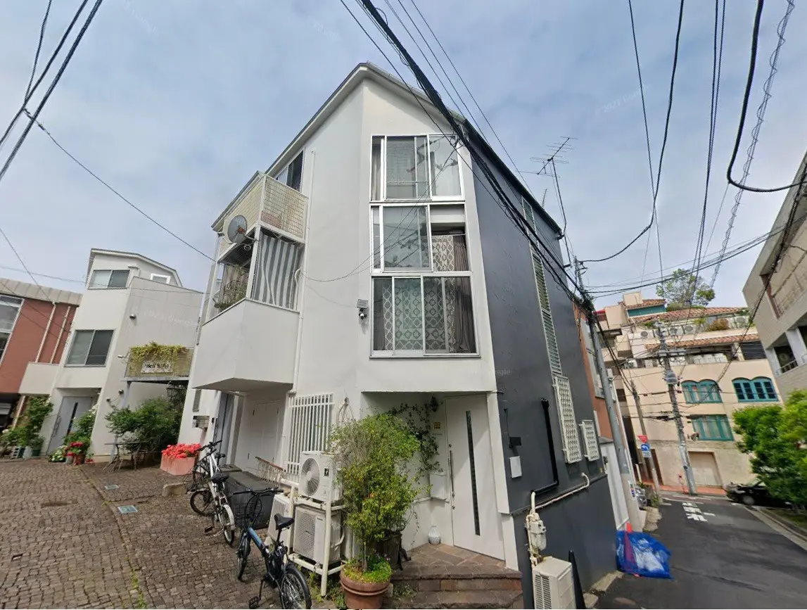 - シンプルな外観の住宅、隣接する建物との狭い路地に面し、自転車と植栽がある風景
