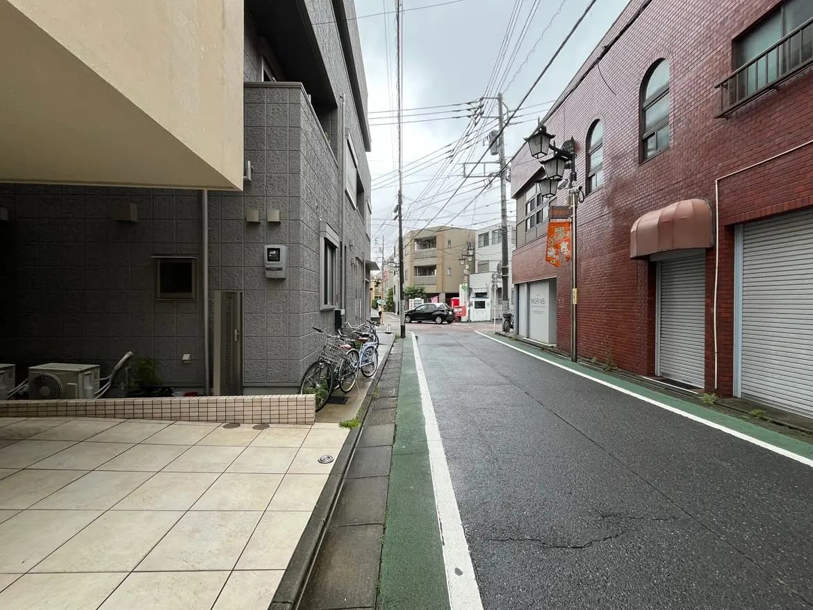 - 雨天の静かな街角、灰色の建物とレンガ造りの壁、歩道と自転車が停まっている風景