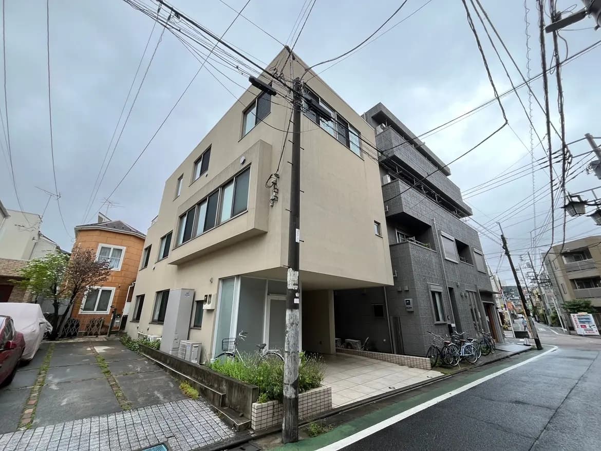 - 現代的なデザインの住宅外観、隣接する建物と電線が見える街の風景
