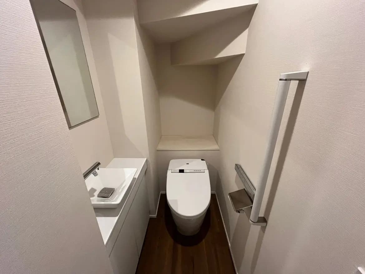 - 白い壁と木目調の床を持つシンプルなトイレ空間、洗面台と鏡が設置された洗面エリアがあるインテリア