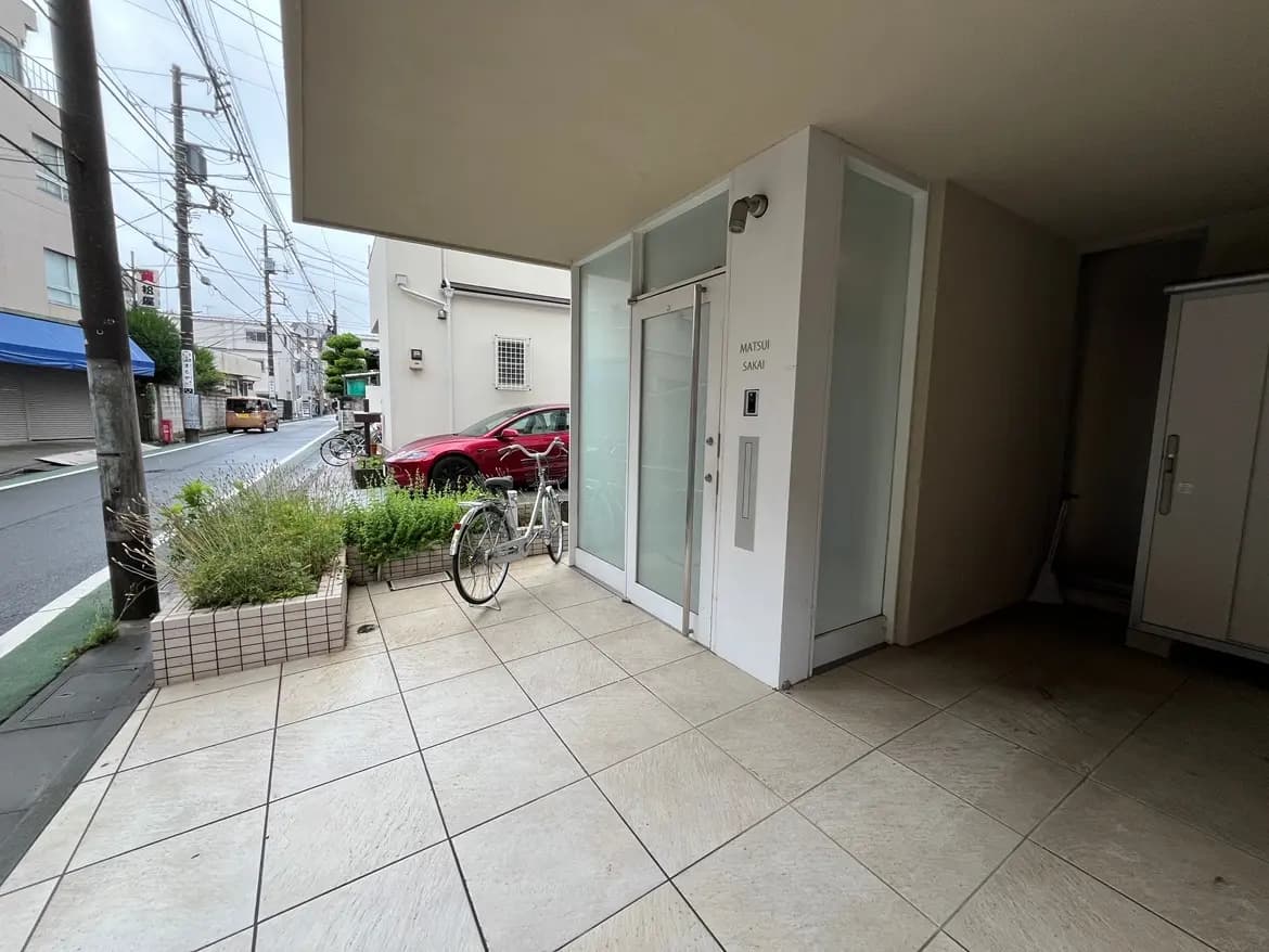 - 自転車が置かれたアパートの入口、手前には植栽があり、寂しい街並みの様子が見える景観
