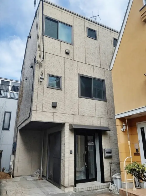 - 現代的なデザインの外観を持つ2階建ての住宅、クリーム色の外壁と大きな窓、隣接する家とのスペースが広がる様子