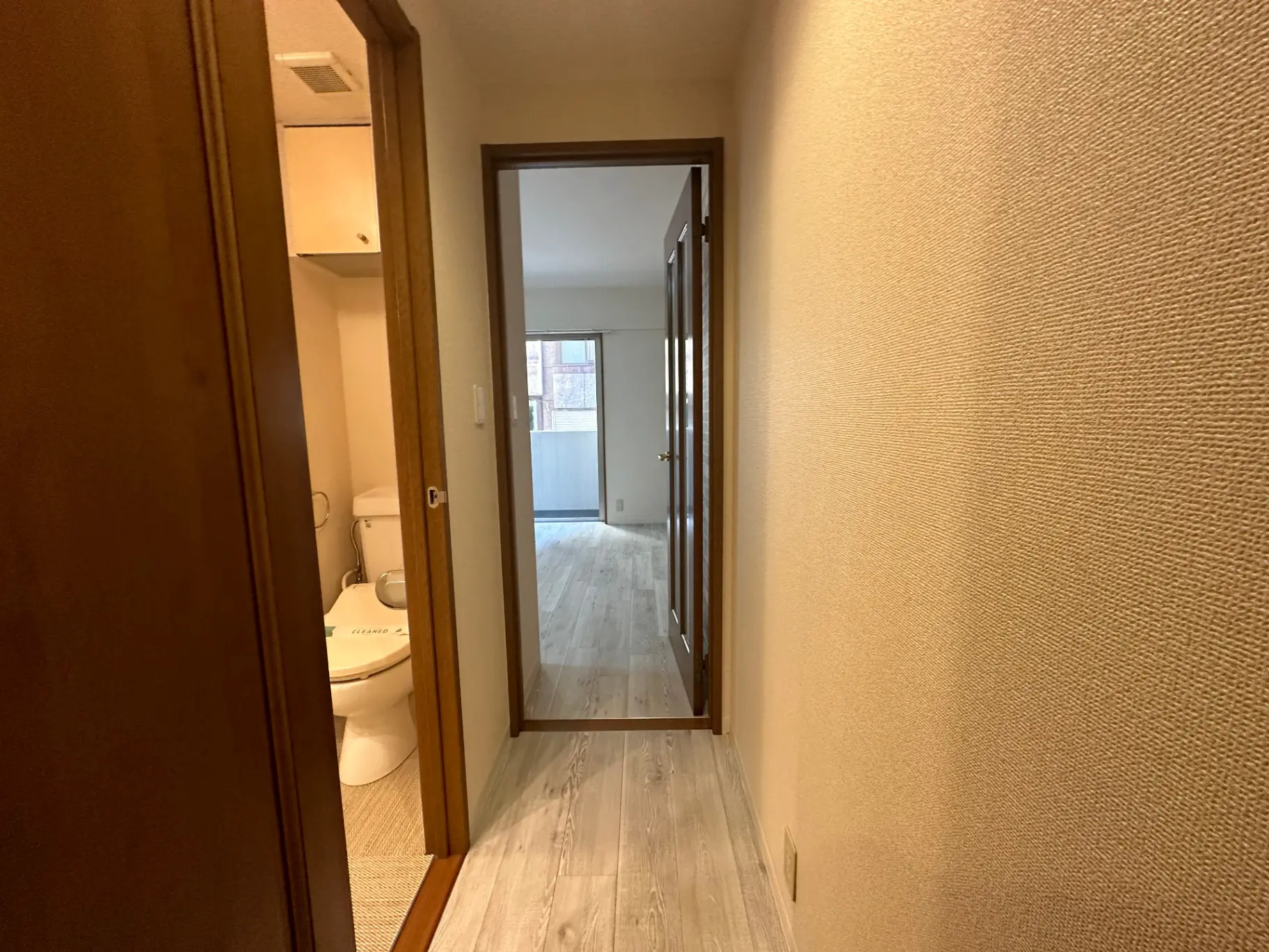 シンプルなデザインの家の中、左にトイレのドア、奥にリビングスペースへつながるガラスドア