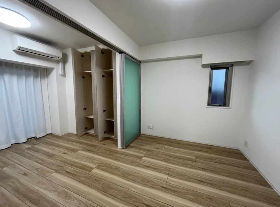 シンプルなデザインの空の部屋、木製フローリング、ビルトインのクローゼットと白いカーテンがついた小窓