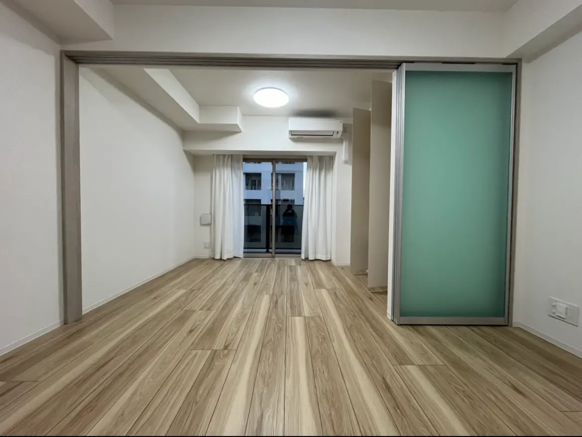 シンプルなデザインの空の部屋、木目調フローリング、スライドドアと白いカーテンのバルコニー付き