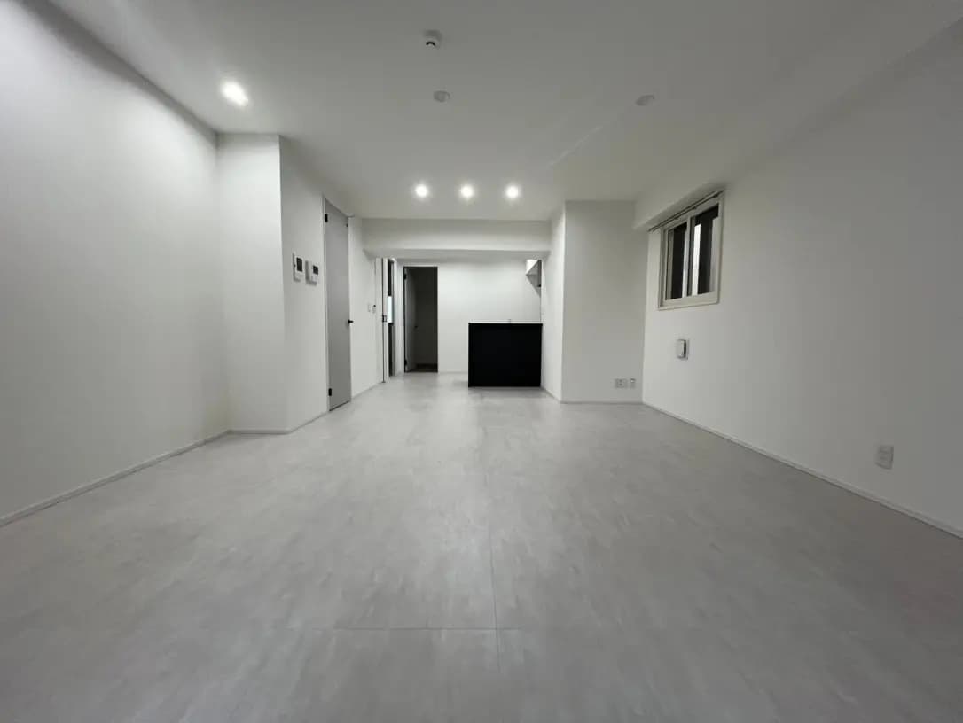 新築のモダンなアパートの内装、ホワイトの壁とグレーのフローリング、LEDダウンライト付きの広々としたリビングルーム