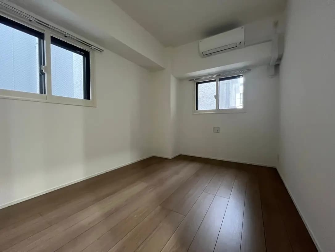 シンプルな内装の空の部屋、木製フローリング、白い壁、二つの窓とエアコンが付いた清潔感のあるインテリア