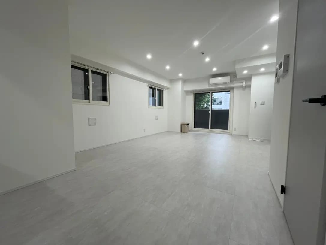 白い壁とグレーのフローリングが特徴的な広々とした空の部屋、天井埋め込み型の照明とエアコンが設置