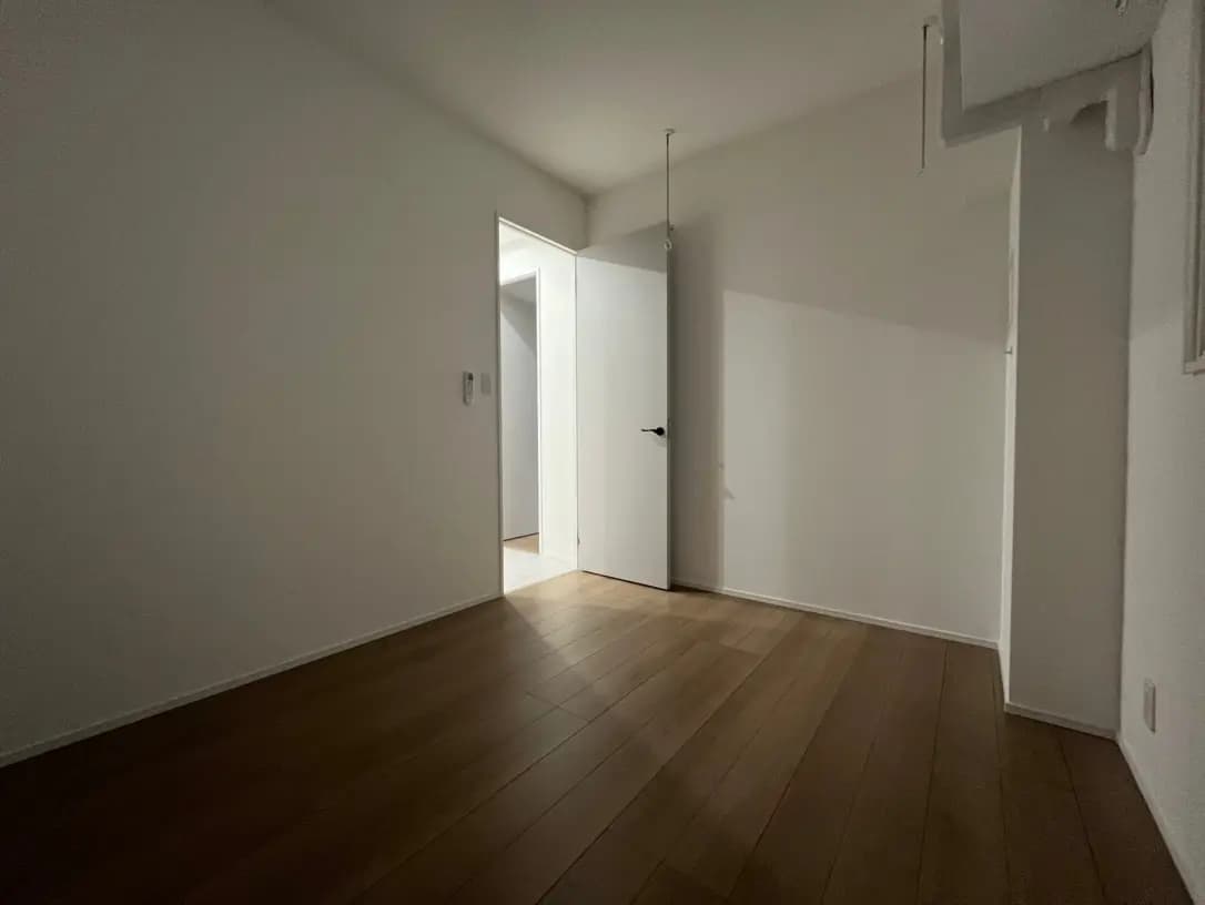 シンプルなデザインの空の部屋、木製のフローリングと白い壁、部屋の左側にドアが見えるインテリア